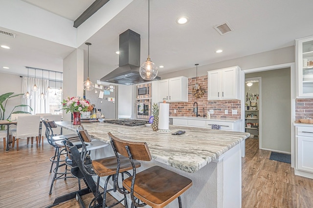 kitchen featuring glass insert cabinets, light stone countertops, island range hood, and white cabinets