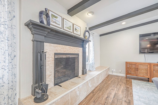 living area featuring beamed ceiling, a tiled fireplace, wood finished floors, and baseboards