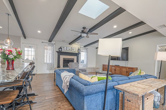 living room featuring beam ceiling, a fireplace with raised hearth, plenty of natural light, and wood finished floors