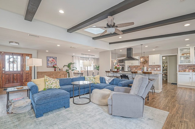 living room with recessed lighting, visible vents, beamed ceiling, and light wood-style flooring