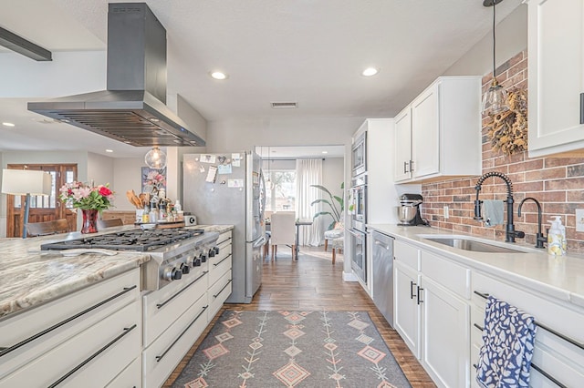 kitchen with hanging light fixtures, appliances with stainless steel finishes, white cabinets, a sink, and island range hood