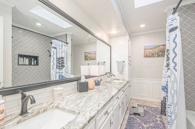 full bathroom with a skylight, crown molding, a sink, and a wainscoted wall