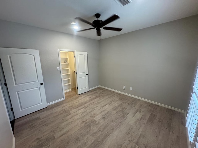 unfurnished bedroom with light wood-type flooring, a closet, a spacious closet, and ceiling fan