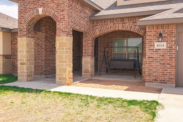 doorway to property featuring roof with shingles and brick siding