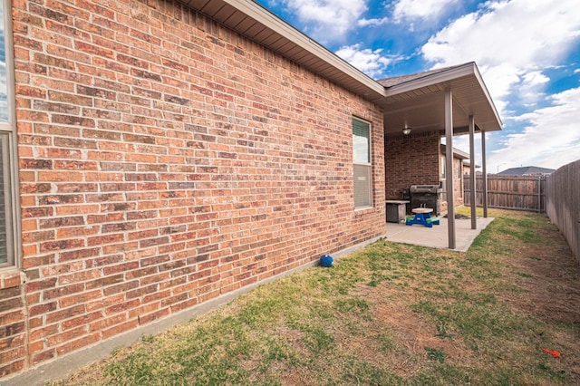 view of side of home featuring a patio, brick siding, a fenced backyard, and a lawn