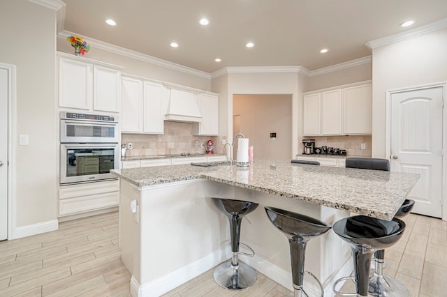 kitchen featuring double oven, a breakfast bar area, black electric stovetop, a spacious island, and premium range hood