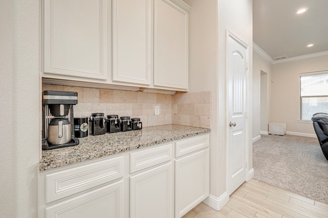 kitchen featuring light stone counters, tasteful backsplash, crown molding, white cabinets, and baseboards