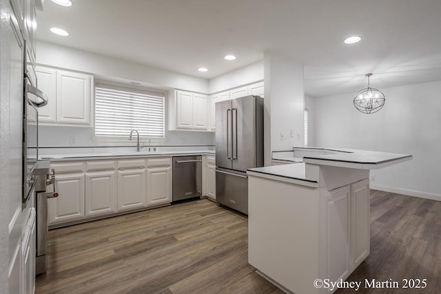 kitchen with appliances with stainless steel finishes, a sink, white cabinets, dark wood-type flooring, and a peninsula