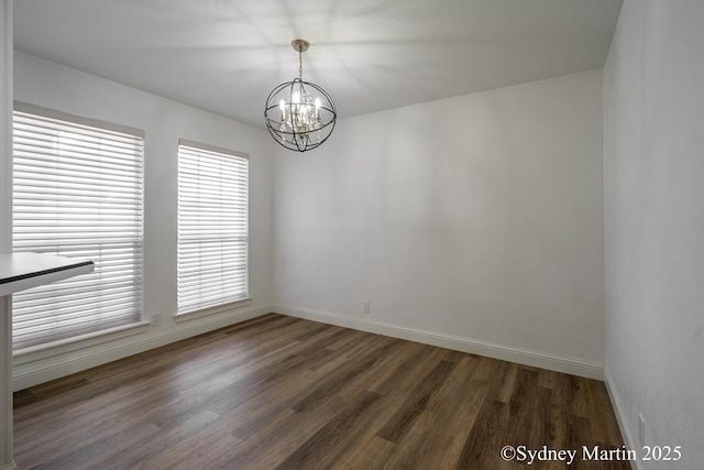 empty room featuring a chandelier, baseboards, and dark wood-type flooring