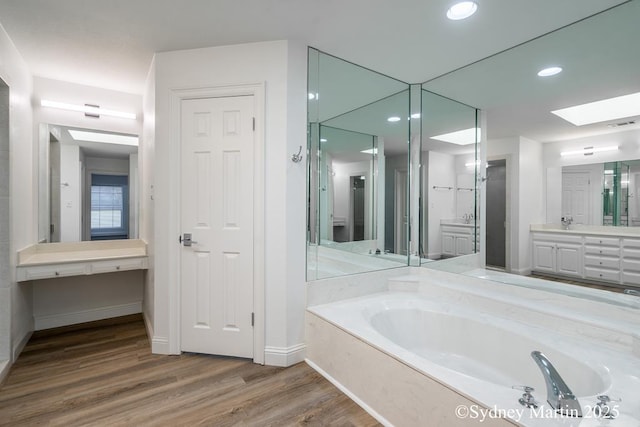 full bathroom featuring a skylight, wood finished floors, a garden tub, vanity, and recessed lighting