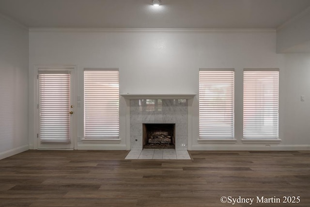 unfurnished living room featuring crown molding, wood finished floors, a tiled fireplace, and baseboards