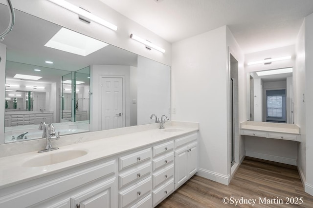 bathroom featuring wood finished floors, baseboards, double vanity, and recessed lighting