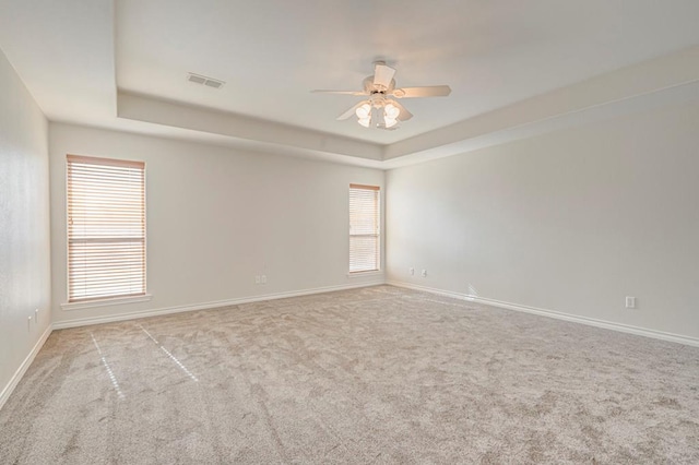 carpeted spare room featuring a raised ceiling and ceiling fan