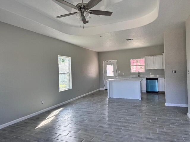 interior space with dishwasher, sink, dark wood-type flooring, a tray ceiling, and white cabinets