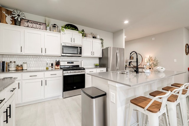 kitchen with a breakfast bar area, stainless steel appliances, backsplash, white cabinets, and a sink