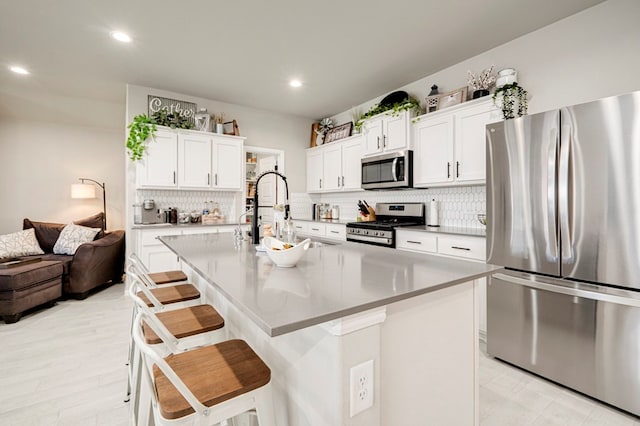 kitchen with stainless steel appliances, a sink, white cabinetry, decorative backsplash, and a kitchen bar