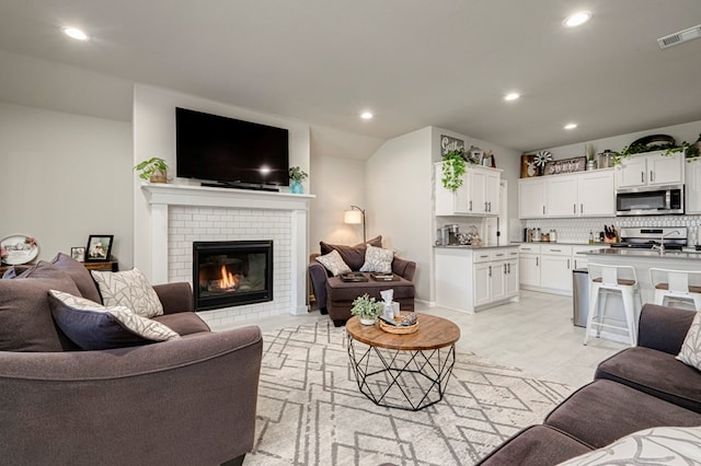 living area with a brick fireplace, visible vents, and recessed lighting