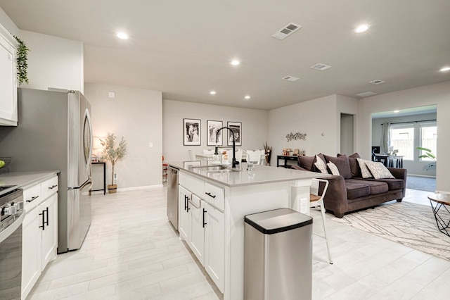 kitchen with a center island with sink, visible vents, white cabinets, stainless steel appliances, and a sink