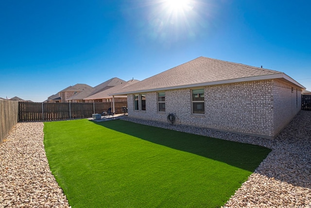 rear view of house with a shingled roof, brick siding, a yard, and a fenced backyard