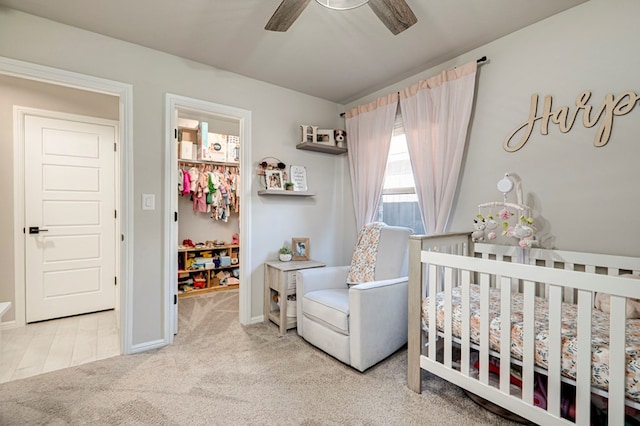 carpeted bedroom with a nursery area, ceiling fan, and baseboards