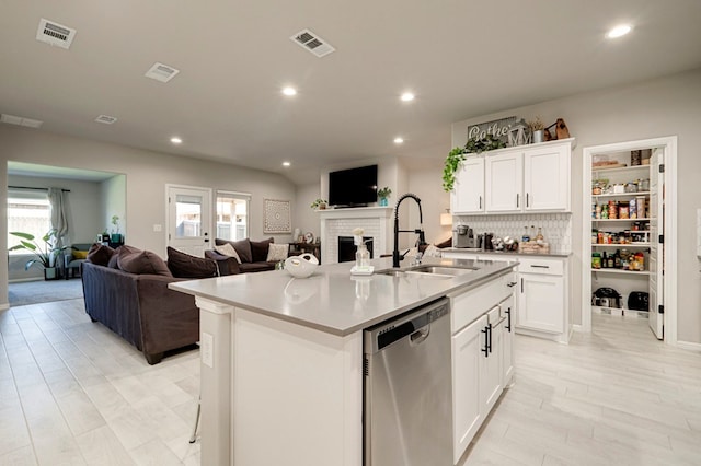 kitchen with a fireplace, stainless steel dishwasher, open floor plan, a sink, and an island with sink