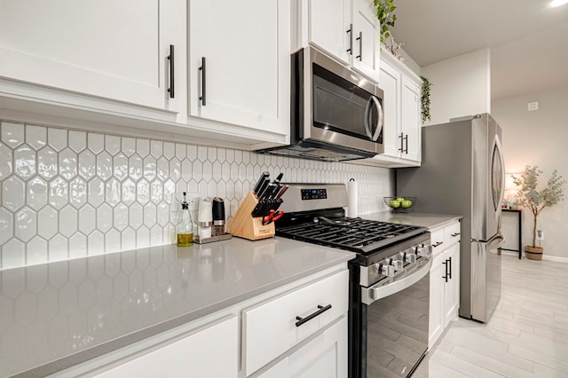 kitchen featuring light wood finished floors, appliances with stainless steel finishes, white cabinets, and decorative backsplash