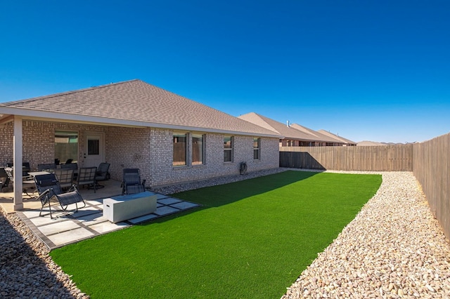 back of property with brick siding, a patio, a fenced backyard, and a lawn