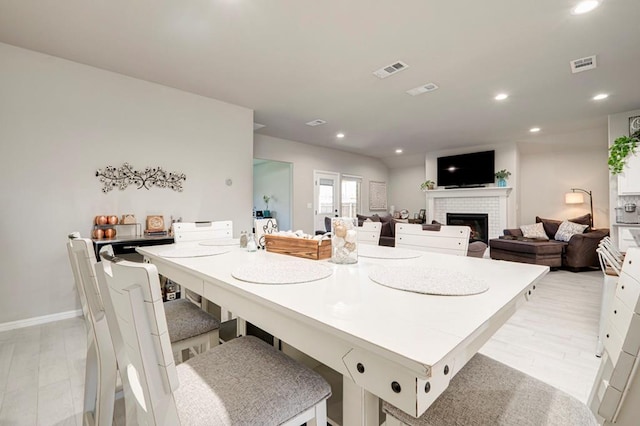 dining space with light wood-type flooring, recessed lighting, a brick fireplace, and visible vents