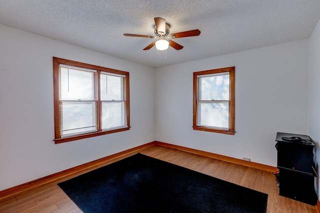 empty room with ceiling fan, a healthy amount of sunlight, a textured ceiling, and hardwood / wood-style flooring