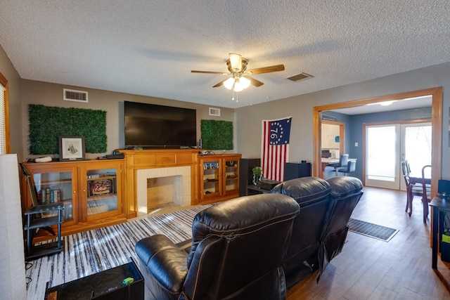 living room with ceiling fan, wood-type flooring, a textured ceiling, and a tiled fireplace