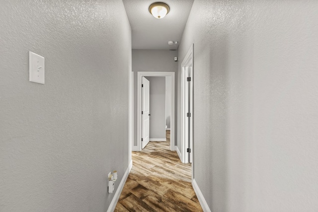 hall with light wood-style floors, a textured wall, and baseboards