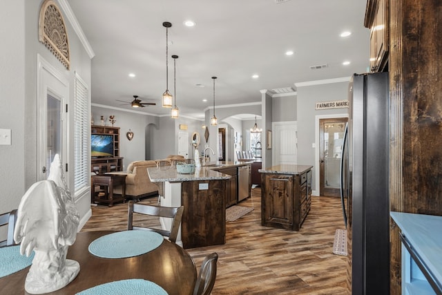 kitchen featuring arched walkways, visible vents, appliances with stainless steel finishes, a center island with sink, and pendant lighting