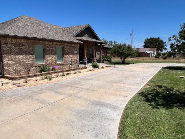 single story home with concrete driveway, brick siding, a front lawn, and roof with shingles