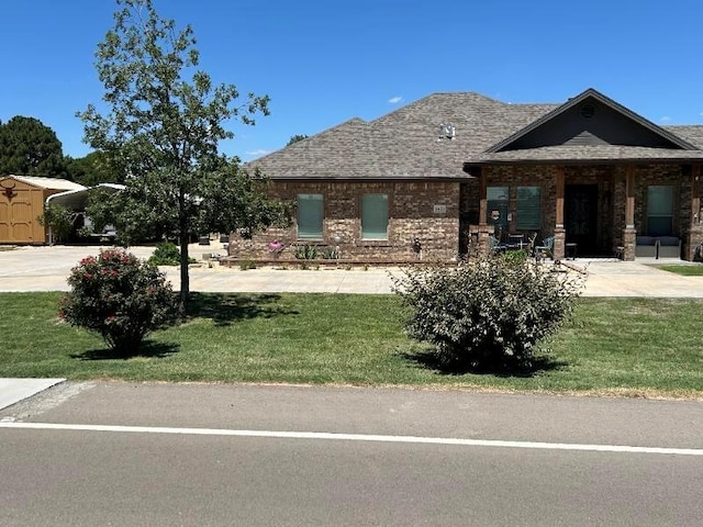 view of front of home with a shingled roof, a front lawn, and brick siding