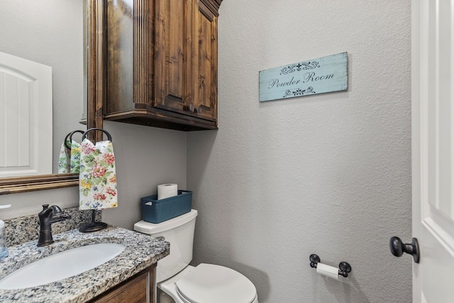 bathroom featuring toilet, a textured wall, and vanity