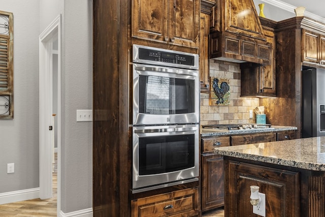 kitchen with dark brown cabinetry, light stone countertops, stainless steel appliances, and backsplash