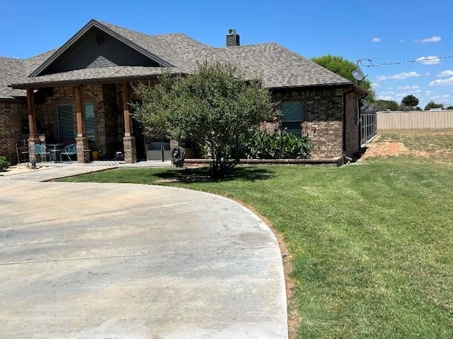 view of front of house featuring brick siding, a chimney, a patio area, fence, and a front lawn