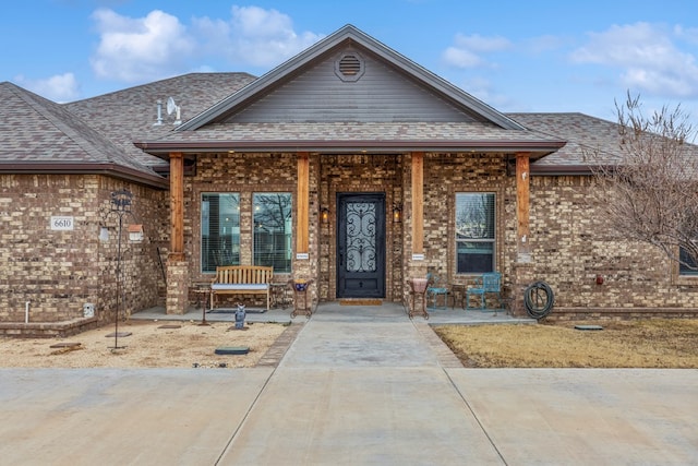 view of front of property featuring covered porch, brick siding, and roof with shingles