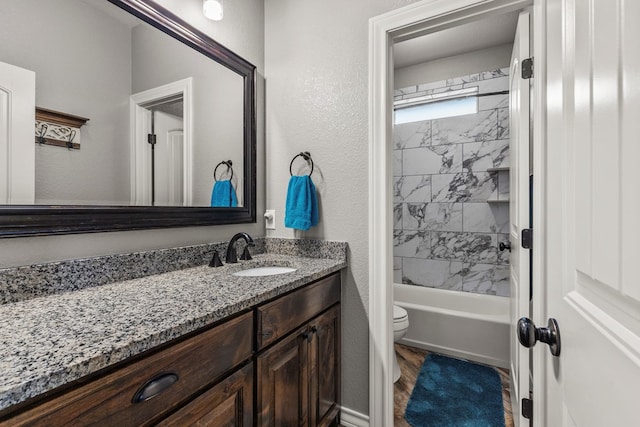 bathroom featuring toilet, a textured wall, washtub / shower combination, and vanity