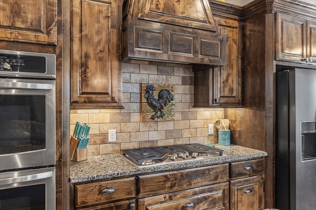 kitchen featuring stainless steel appliances, dark brown cabinets, dark stone countertops, and backsplash