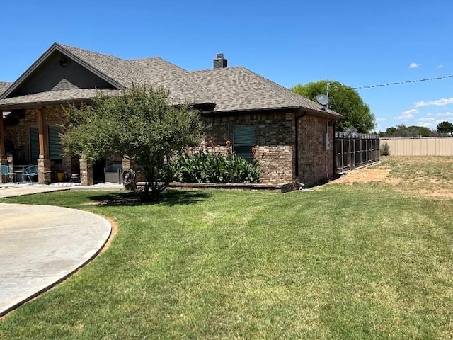 view of side of home with roof with shingles, brick siding, a lawn, and fence