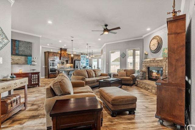 living room with recessed lighting, ornamental molding, light wood-type flooring, a fireplace, and ceiling fan with notable chandelier