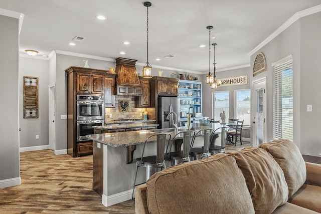 kitchen with stainless steel appliances, a kitchen breakfast bar, hanging light fixtures, an island with sink, and dark stone countertops