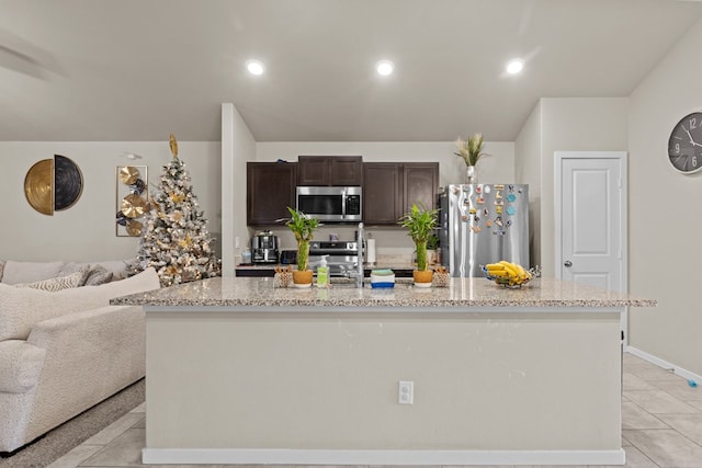 kitchen featuring light stone counters, an island with sink, dark brown cabinets, light tile patterned floors, and appliances with stainless steel finishes