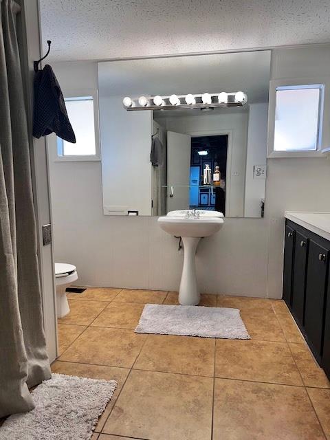 bathroom featuring toilet, tile patterned flooring, and a textured ceiling