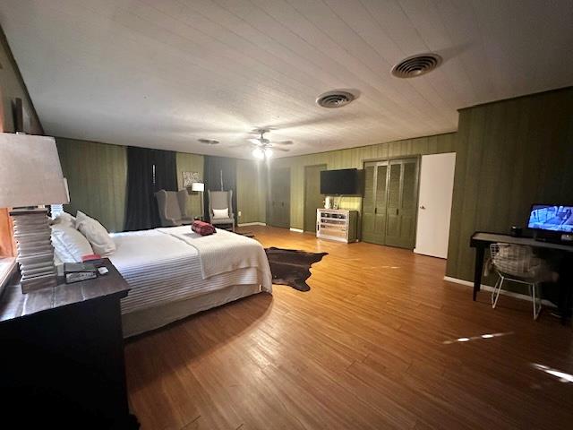 bedroom with hardwood / wood-style flooring, ceiling fan, and wood walls