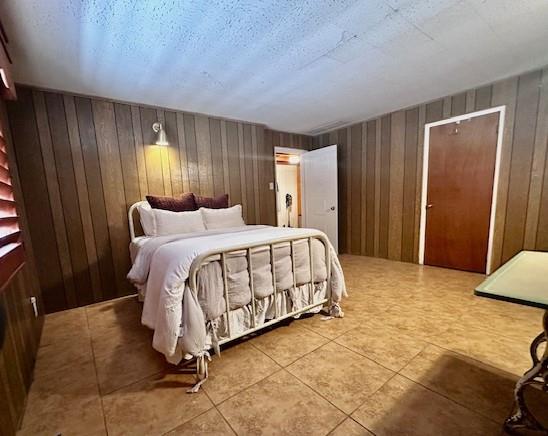 bedroom with tile patterned flooring, a textured ceiling, and wood walls