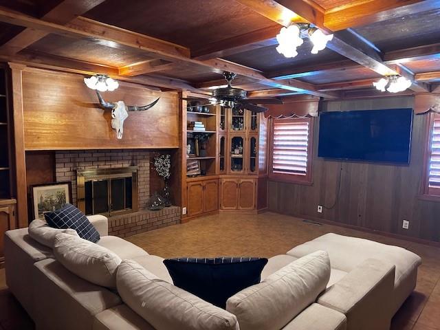 living room featuring coffered ceiling, a brick fireplace, beamed ceiling, and wood walls