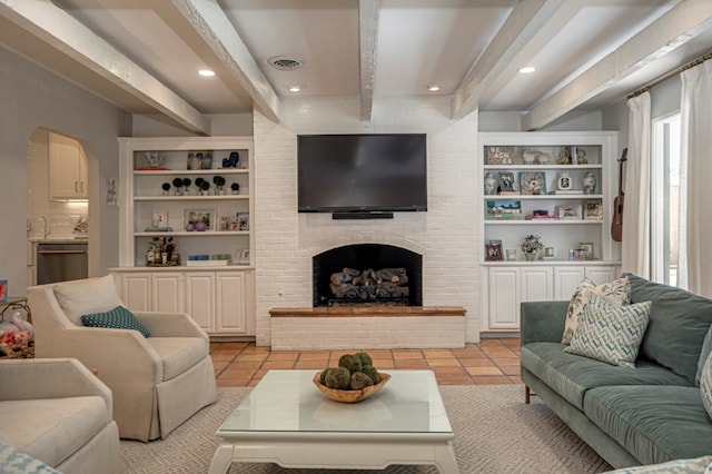 living room featuring beam ceiling, built in shelves, light tile patterned flooring, and a brick fireplace