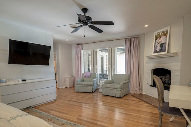 living room with ceiling fan, light hardwood / wood-style floors, and a brick fireplace